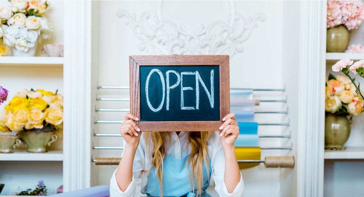Self Employed image showing a woman holding up a blackboard with the word open in a pretty shop