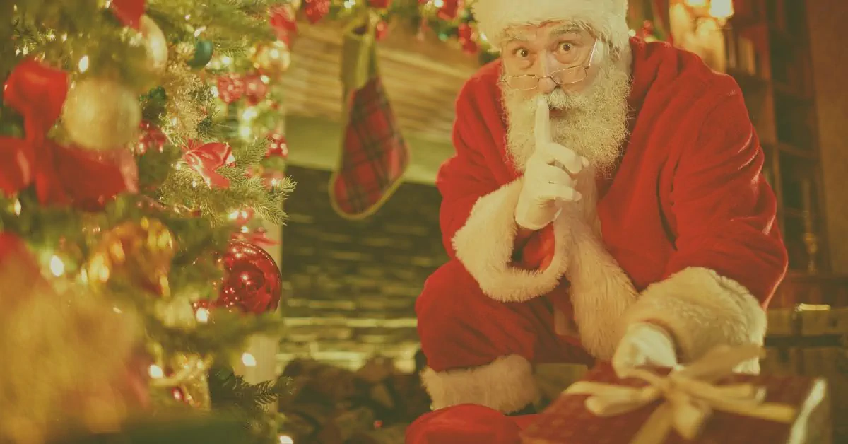 Santa Claus in red suit quietly shushing with finger to lips while placing gifts under a twinkling Christmas tree beside a cosy fireplace – perfect fibro-friendly festive magic.